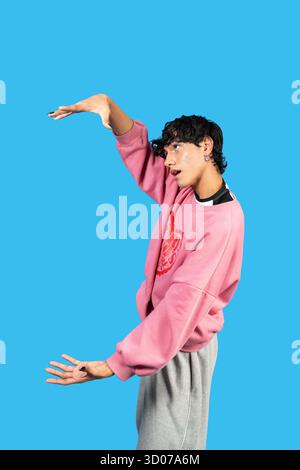 Jeune homme posant de manière ludique dans un sweat-shirt rose sur un fond bleu Banque D'Images