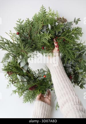 Couronne de Noël élégante pour l'intérieur, accrochez la couronne sur la porte. Fait à la main, la jeune fille tient une couronne fraîchement faite dans ses mains. L'atmosphère de Banque D'Images