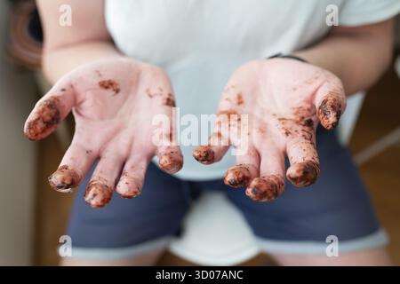 L'homme montre ses mains, tous les doigts couverts de chocolat fondu. Amusement, anniversaire, vacances, fête Banque D'Images