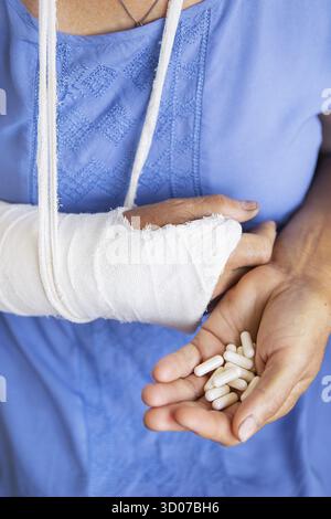 Une femme âgée à la retraite avec un bras de réenroulement dans une coulée et un bandage contient des pilules anesthésiques. Coup, fracture, os, hôpital Banque D'Images