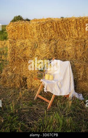 Pique-niquez dans le champ près des balles de paille. Le soleil couchant. Style rustique - chaise en bois, écossais, bouquet de fleurs, bougies Banque D'Images