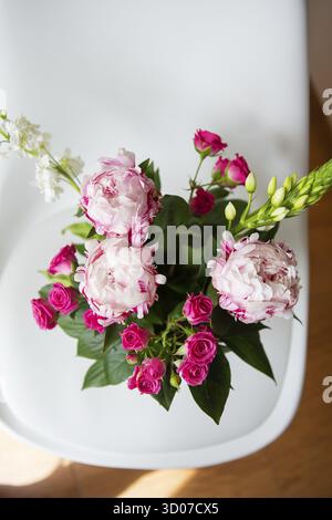 Un beau bouquet de pivoines roses tendres et de petites roses se dresse sur une chaise blanche. Idéal pour un bouquet de mariée, un anniversaire. Gros plan, vue de dessus Banque D'Images