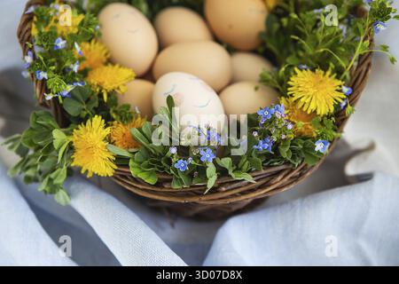 Beau bouquet de printemps dans un panier en bois où se trouvent les oeufs peints de Pâques, un oeuf avec un visage mignon Banque D'Images