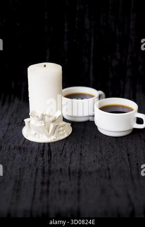 Bougie et deux tasses de café sur fond noir Banque D'Images