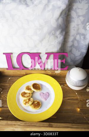 Crêpes au fromage sur une assiette jaune se tiennent sur un plateau en bois avec une bougie et des lumières Banque D'Images