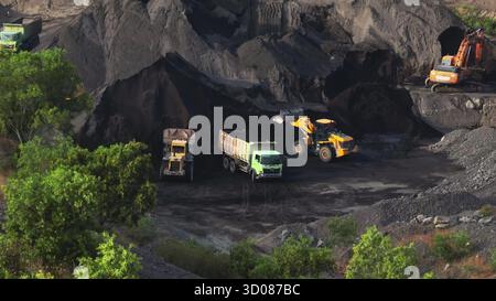 Excavatrice et chargeuses sur pneus chargement de tombereaux à benne basculante avec du charbon brut dans une vaste mine à ciel ouvert, machines lourdes extrayant des combustibles fossiles pour le traitement industriel et la production d'énergie. Concept industriel Banque D'Images