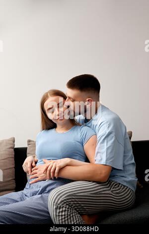 Le couple attend profite d'un moment tendre sur le canapé, célébrant leur amour et l'anticipation d'accueillir une nouvelle vie dans leur famille Banque D'Images
