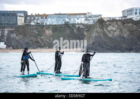 DATE DE CORRECTION RETRANSMISE les paddleboarders du Newquay Activity Centre entrent dans l'esprit d'Halloween lors d'une pagaie tôt le matin à l'aube à travers Newquay Bay à Cornwall, où les amateurs de sports nautiques préparent des tenues pour une semaine de célébration des activités dans la ville balnéaire pendant Spooky Newquay pendant les vacances d'Halloween, à partir du samedi 25 octobre. Date de la photo : mercredi 22 octobre 2025. Banque D'Images