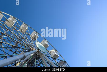 Grande roue se tient contre le ciel bleu. Grande attraction de carnaval en métal avec cabines rotatives offre parc d'attractions d'été aventure de loisirs, imposante ci Banque D'Images