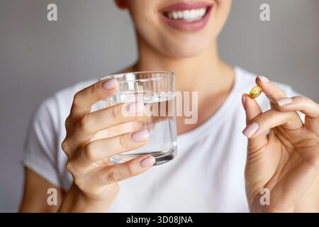 Gros plan de belle main de femme tenant des vitamines colorées et des pilules sur Palm. Fille tenant des comprimés, capsules et verre d'eau douce. Vitamine et alimentation Banque D'Images