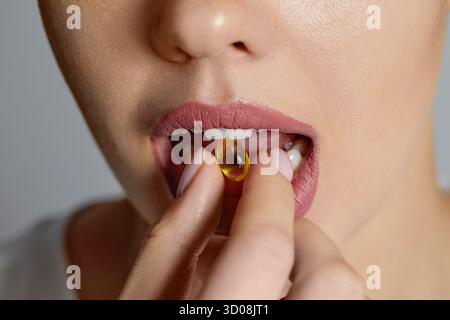 Vitamine et supplément. Gros plan de belle jeune femme prenant Yellow Fish Oil Pill. Main féminine mettant Omega-3 capsule dans la bouche. Alimentation saine et Banque D'Images