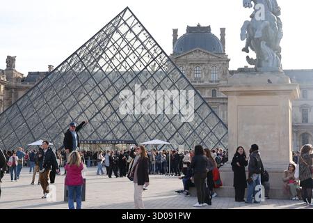 Paris, France. 22 octobre 2025. Les touristes sont photographiés devant la pyramide du Louvre à Paris, France, 22 octobre 2025. Le musée du Louvre a rouvert aux visiteurs mercredi matin, trois jours après un vol de bijoux qui a causé des pertes considérables. Crédit : Zhang Baihui/Xinhua/Alamy Live News Banque D'Images