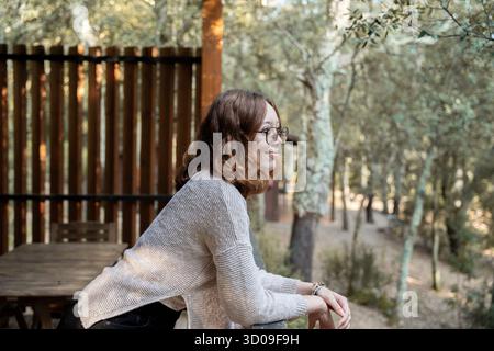 Femme debout sur une terrasse en bois embrassant un mode de vie sain dans une cabane forestière Banque D'Images