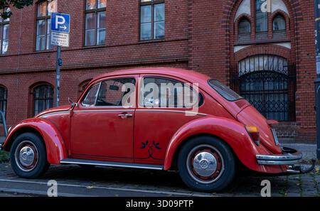 Rouge vintage Volkswagen Beetle garé sur une rue de Berlin devant une façade historique en briques. Banque D'Images