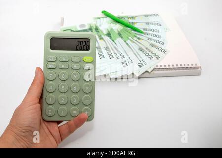 Calculatrice montrant l'année 2026 avec des billets en euros et stylo vert sur fond blanc. Concept de planification financière, d'objectifs commerciaux et de budget pour le Banque D'Images