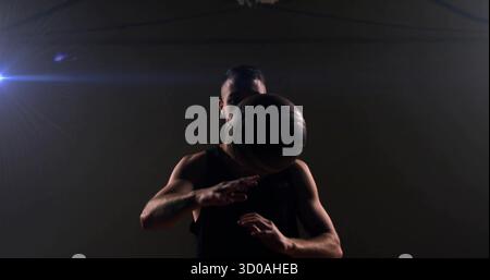 Athlète masculin dribble portant une chemise noire sans manches à la salle de gym, avec basket-ball, projecteurs plafonniers Banque D'Images