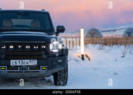 Mourmansk, Russie - 13 décembre 2024 : gros plan de l'extrémité avant du Jetour T2 à côté d'un poteau lumineux éclairé. Vue frontale rapprochée des phares et du VUS Banque D'Images