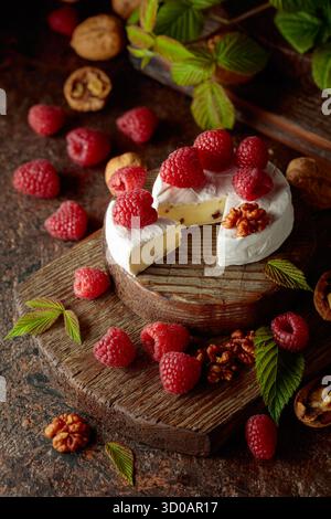 Camembert avec framboises fraîches et noix sur une table vintage brune. Banque D'Images