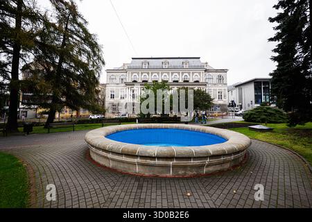 Tarnow, Pologne - 10 octobre 2025 : fontaine ronde en pierre avec bassin bleu dans un parc près d'un bâtiment historique à Tarnow, Pologne. Banque D'Images