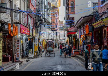 Les gens marchent et font des emplettes le long d’une rue colorée remplie de magasins locaux et de décorations dans le quartier Thamel de Katmandou, Népal – 20 octobre 2025. Banque D'Images