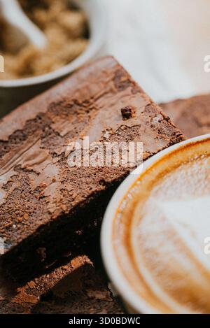 Un brownie se trouve sur une tasse de café. Le brownie est couvert de pépites de chocolat et il est un dessert. Le café est chaud et fumant, et la tasse i Banque D'Images