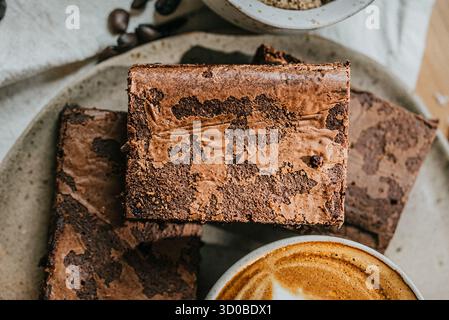 Une assiette de brownies repose sur une table à côté d'une tasse de café. Les brownies sont empilés les uns sur les autres, et le café est surmonté d'un tourbillon de f Banque D'Images