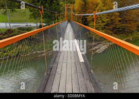 Pont suspendu en bois traversant la rivière en automne. Vue rapprochée d'une étroite passerelle en bois avec des garde-corps orange et des côtés en treillis, enjambant un calme Banque D'Images