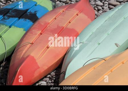 Kayaks en plastique colorés retournés sur une plage de galets à Budleigh Salterton, Devon, Angleterre Banque D'Images