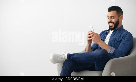 Homme profitant du temps sur smartphone tout en se relaxant dans une chaise confortable à la maison Banque D'Images