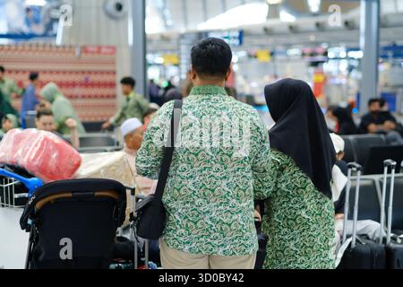 Un couple vêtu de chemises à motifs verts assortis se tient debout avec leurs bagages à l'aéroport. Les membres de leur famille et d'autres voyageurs sont visibles dans le Banque D'Images