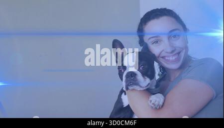 Tenant femme portant un t-shirt gris berçant le chien Boston Terrier à la maison, avec un reflet bleu frais de lentille Banque D'Images