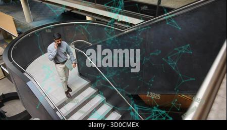 Homme d'affaires ascendant à l'aide d'un smartphone tenant la tablette sur les escaliers courbes dans l'atrium de bureau, espace de copie. Moderne, professionnel, élégant, corporatif, technolog Banque D'Images