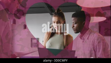 Collaborateurs se réunissant autour d'un ordinateur portable sur une table blanche au bureau, avec une superposition de coeur rose Banque D'Images