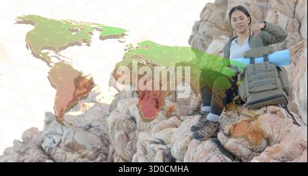 Femme asiatique assise portant du matériel de randonnée sur l'affleurement rocheux de falaise, avec sac à dos et superposition de carte du monde Banque D'Images