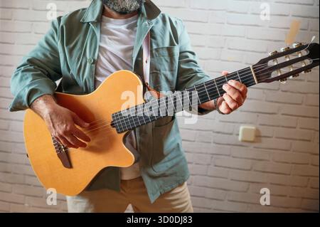 Gros plan d'un homme jouant de la guitare acoustique à l'intérieur. Banque D'Images
