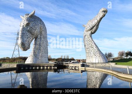 Vue aérienne des Kelpies, deux majestueuses sculptures en tête de cheval reflétées dans les eaux tranquilles sur fond de ciel bleu clair, Falkirk, Écosse, Royaume-Uni. Banque D'Images