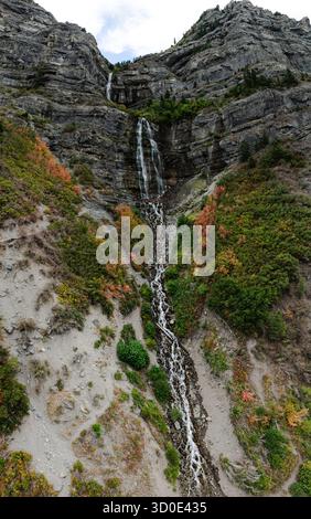 Vue aérienne de Bridal Veil Falls en cascade sur le terrain accidenté, encadrée par les teintes variées du feuillage d'automne contre la paroi rocheuse grise, American Fork, Utah, États-Unis. Banque D'Images