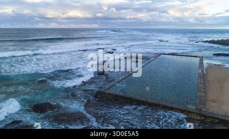 Vue aérienne de la piscine océanique embrassée par des rivages rocheux et des vagues écrasantes sous un ciel nuageux à North Narrabeen, Sydney, Nouvelle-Galles du Sud, Australie. Banque D'Images