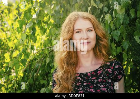 Portrait en gros plan d'une charmante dame avec de longs cheveux de gingembre rouge et des taches de rousseur souriant regardant la caméra dans le parc en été. Les gens dans la nature et le bonheur co Banque D'Images