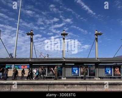 Haïfa, Israël, 2 octobre 2025, Gare de Hashmona. Des gens et deux soldats se tiennent sur un quai de train avec des affiches commerciales sur le mur de l'abri. Banque D'Images