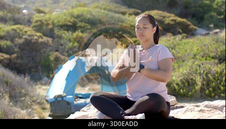 Femme en top rose et leggings méditant sur le rocher de camping, avec tente, sac à dos, recouvrement globe Banque D'Images