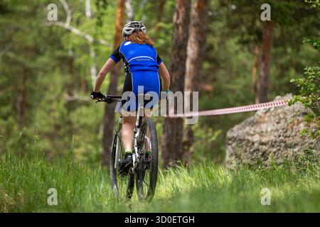 Vue arrière femme chevauchant VTT dans la forêt à côté d'un grand rocher Banque D'Images