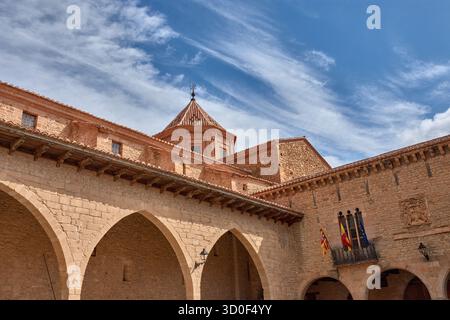 La place Cristo Rey à Cantavieja se caractérise par son architecture médiévale en pierre avec des arches et des balcons ornés de drapeaux. Les tons chauds de th Banque D'Images