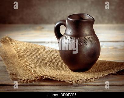 Cette photographie en gros plan capture les magnifiques détails d'un pichet vintage aux côtés d'une serviette en toile de jute rustique, parfaite pour mettre en valeur la maison classique de Banque D'Images