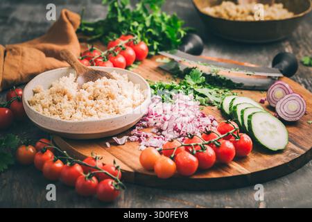 Ingrédients pour salade de couscous tabouleh maison avec légumes frais et herbes sur planche à découper Banque D'Images