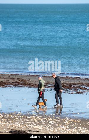 couple plus âgé ou d'âge moyen promenant leur petit chien sur une plage de l'île de wight à marée basse. homme et femme promenant chien au bord de la mer. Banque D'Images
