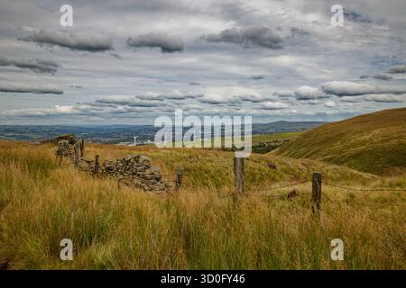 Un mur de pierres sèches et des poteaux de clôture dans un paysage montagneux regardant vers un parc éolien sur le bord d'une ville dans une vallée, Burnley, Lancashire. Banque D'Images