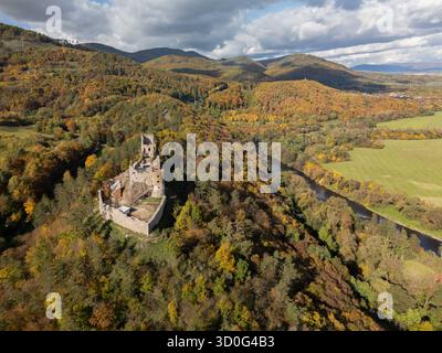 Vue aérienne d'une ruine de château médiéval nichée parmi les forêts aux couleurs d'automne à côté d'une rivière sinueuse, Revistske Podzamcie, Banskobystricky kraj, Slovaquie. Banque D'Images