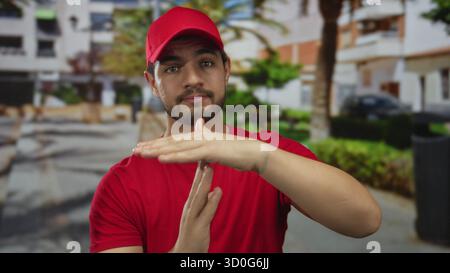 Homme en casquette rouge et t-shirt fait un geste de timeout avec les mains à côté de sa poitrine dans un cadre de parc vert ; calme. Banque D'Images