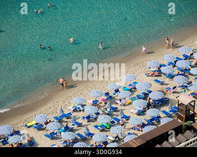 Vue aérienne de la plage où les eaux turquoises rencontrent le sable doré, parsemée de parasols bleus et blancs, Cefalù, Sicile, Italie. Banque D'Images